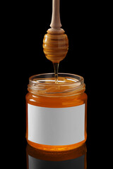 Honey dripping from dipper into full glass jar with white blank label isolated on black background. Product mock up.