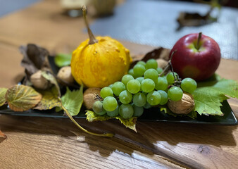 a plate with autumn fruits (grapes, apple, pumpkin and nuts)