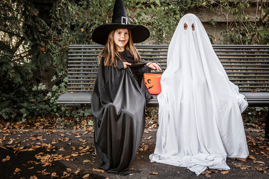 Bed sheet ghost and witch sitting on bench