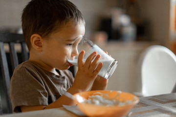 boy in the kitchen at home having breakfast and eating porridge and drinking milk 