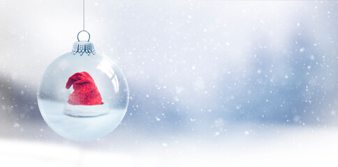Gläserne Weihnachtskugel mit Weihnachtsmann vor unscharfem Blauem Hintergrund mit Schneeflocken