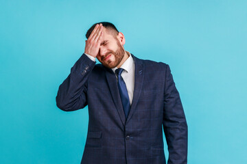 Portrait of upset bearded man wearing official style suit standing with facepalm gesture, blaming...