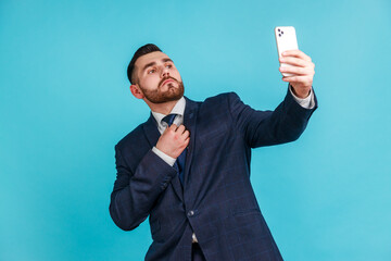 Portrait of self-confident man with beard wearing official style suit straighten a tie and making...