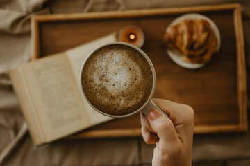 Female hand holding cup of coffee while having breakfast reading a book.