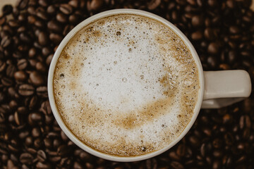 Still Life of cup of coffee at the bottom of the coffee beans on brown background.