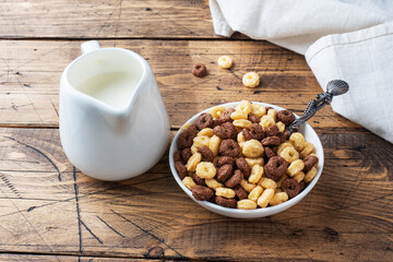 Dry breakfast cereals. Chocolate and corn rings made from natural cereals with milk in a plate. Wooden rustic background, copy space.