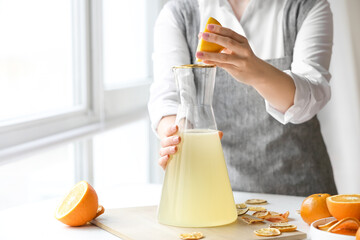 Woman making fresh citrus juice at table in kitchen