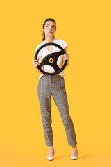 Fototapeta premium Thoughtful young woman with steering wheel on color background