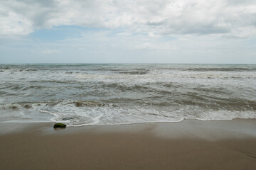 Waves of the Sea Reaching the Shore with Lots of Foam in a Cloudy and Cold Sky