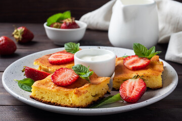 Cottage cheese casserole with strawberries and mint. Delicious homemade dessert made of curd and fresh berries with cream. dark wooden background, copy space.