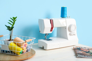 Modern sewing machine on table near blue wall