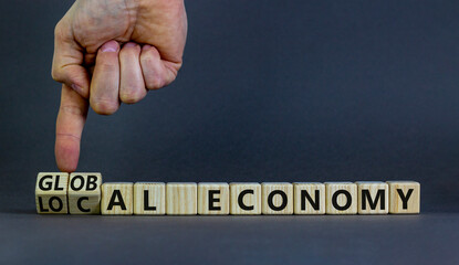 Local or global economy symbol. Businessman turns wooden cubes and changes words 'local economy' to 'global economy'. Beautiful grey background. Business, local or global economy concept. Copy space.