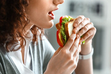 Young businesswoman eating tasty sandwich in office, closeup - Powered by Adobe