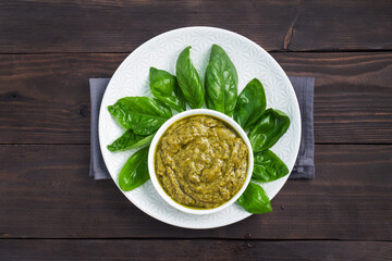 Pesto sauce in a plate and fresh basil leaves with garlic. dark wooden background, copy space.