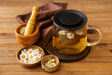 Teapot of tasty chamomile tea and flowers on wooden background