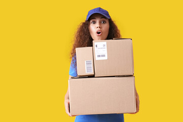 Surprised African-American courier with parcels on color background