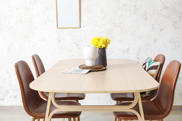 Fototapeta na wymiar Dining table with flowers in vase and chairs near light wall