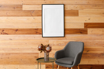 Blank poster frame on wooden wall in interior of modern room with armchair
