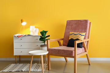 Interior of room with stylish armchair, white chest of drawers and table near color wall