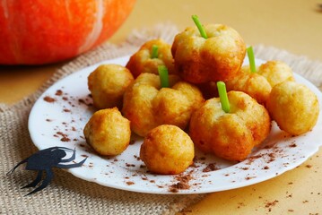 Halloween food. Fried flour donuts in the shape of a pumpkin and a green handle on a white plate with a canvas napkin next to a paper spider decor. Purchase plan.