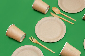 Recyclable fork, spoon, knife, plate and cup on a green background. Kitchen utensils are served on the table. Top view. Minimalist Style. Copy space