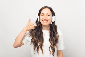 Wide smiling woman is listening to audio book, podcast or music through earphones and showing thumb up.