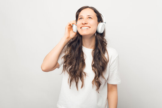 Dreamy young woman enjoys using her earphones over white background.