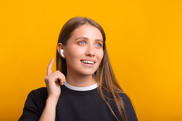 Beautiful woman is wearing some wireless ear pods over yellow background.