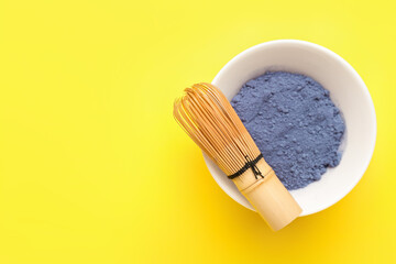 Bowl of powdered blue matcha tea and chasen on yellow background