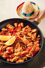 Frying pan with tasty Fajita and sombrero hat on light background