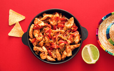 Frying pan with tasty Fajita, nachos and sombrero hat on color background