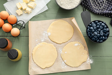 Raw dough with ingredients for blueberry galettes on color wooden background