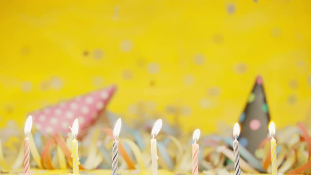 Party decoration burning candels party hats streamers raing confetti isolated on yellow background shot in 4k super slow motion