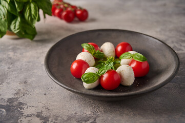 Delicious caprese salad with ripe tomatoes, fresh basil and mozzarella cheese in black plate on the background as concrete. Close up 