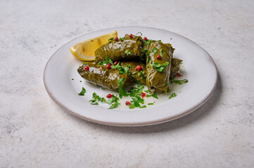 Stuffed grape leaves with rice, meat, parsley, pepper and lemon in white plate. Top view dolma. Light wooden background, close up