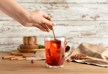 Woman preparing tasty cranberry tea on wooden table