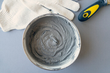 Worker equipment: container with cement, putty knife and workers gloves on a desk, top view