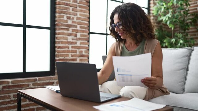 Middle age hispanic woman doing countability with documents and laptop