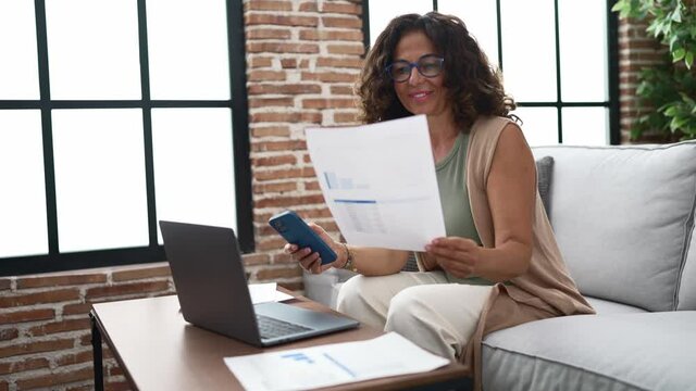 Middle age hispanic woman doing countability with documents and laptop