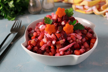 Salad Vinaigrette with beets, potatoes, carrots, squid, pickles and vegetable oil on light blue background.