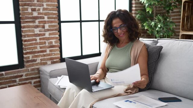 Middle age hispanic woman doing countability with documents and laptop
