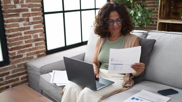 Middle age hispanic woman doing countability with documents and laptop