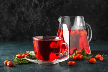 Glass cup of tasty rose hip tea and berries on black background