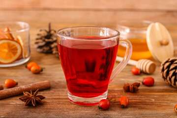 Glass cup of tasty rose hip tea and berries on wooden background