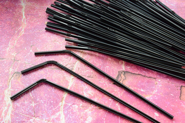 Several dozen striped black cocktail tubes scattered against a pink marble backdrop
