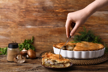 Woman eating piece of tasty chicken pot pie on wooden background