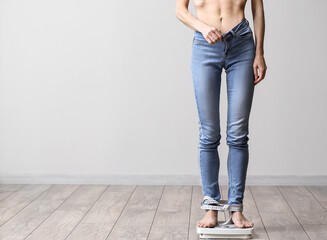 Young woman with anorexia measuring her weight on grey background