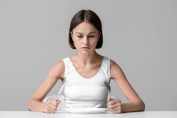 Young woman with empty plate at table. Anorexia concept