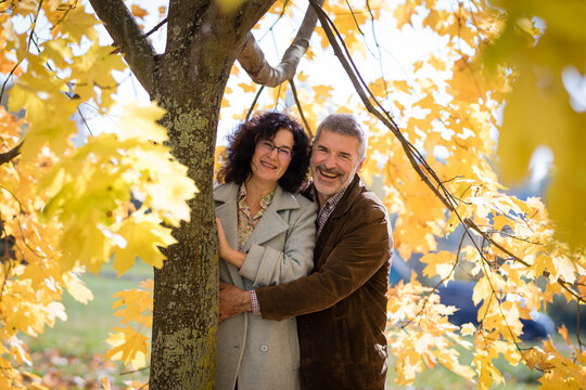 Portrait Of A Mature Couple 50 Years Old In An Autumn Park. Man And Woman Embracing And Looking At The Camera And Smiling