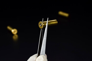 Hand in exam gloves keeping bullet with tweezers, inspection of crime evidence black background.         